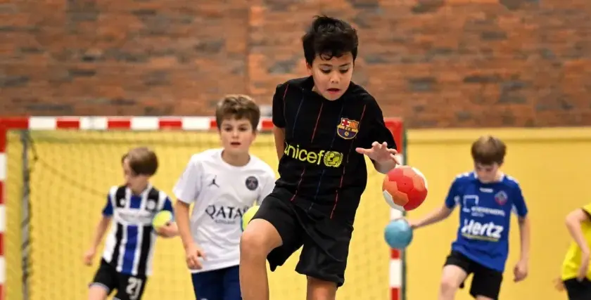 Jungen in Sporttrikots spielen Staffelspiele mit Ball in einer Sporthalle.