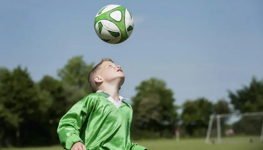 Junge im grünen Trikot übt den Kopfball. Der Ball schwebt über ihm, bereit für den perfekten Treffer.