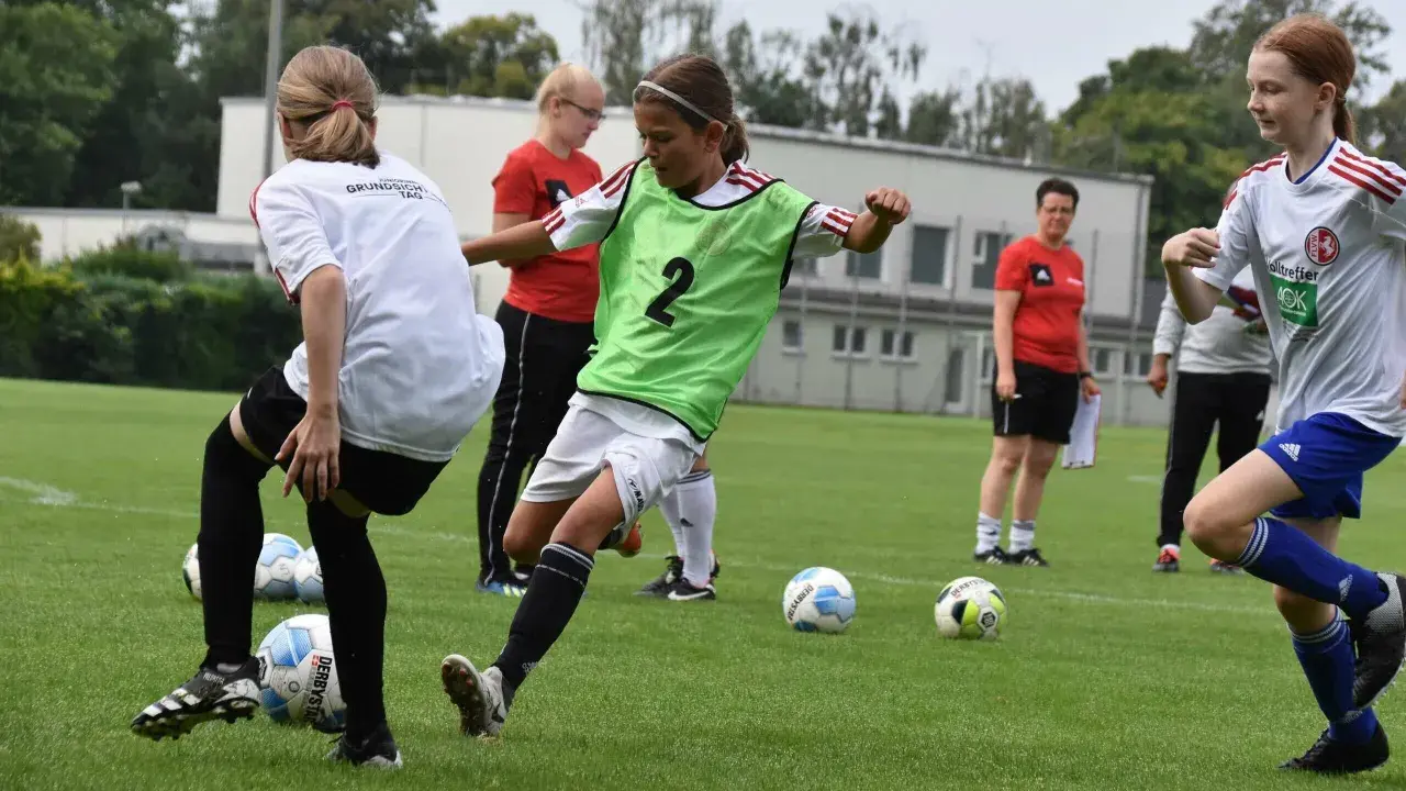 Mädchen im **Jugend Fußball** Training üben Dribblings. Ein Mädchen mit grüner Weste und der Nummer 2 am Ball.