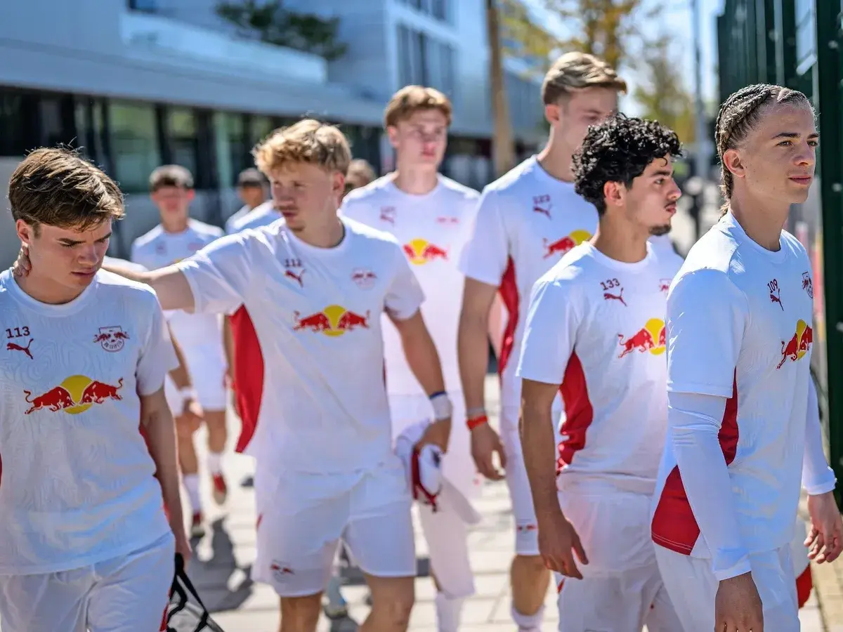 Junge Fußballer des RB Leipzig U12 Teams in weißen Trikots mit dem Bullen-Logo gehen gemeinsam.