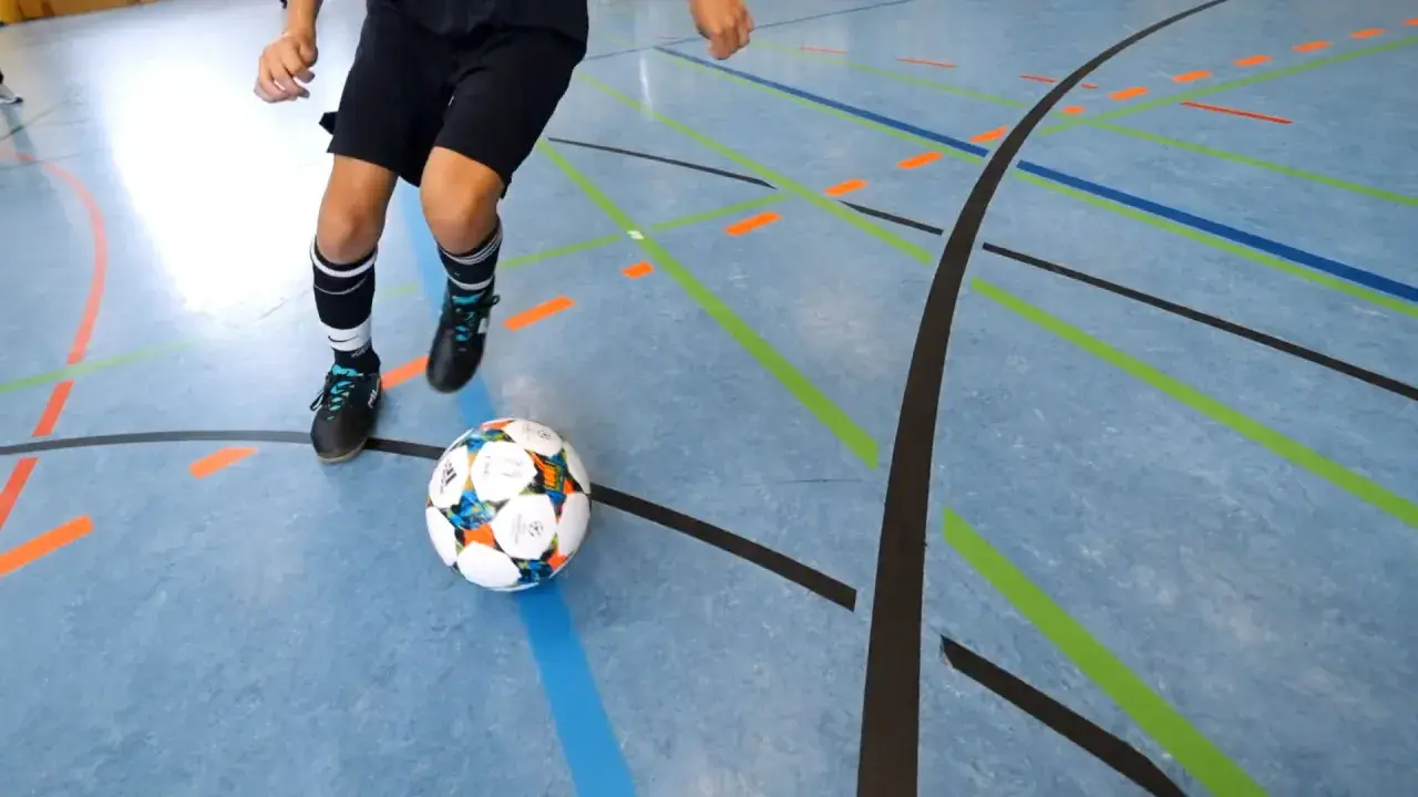 Ein Spieler übt Dribblings auf dem Hallenboden, die Linien markieren die Futsal Positionen.