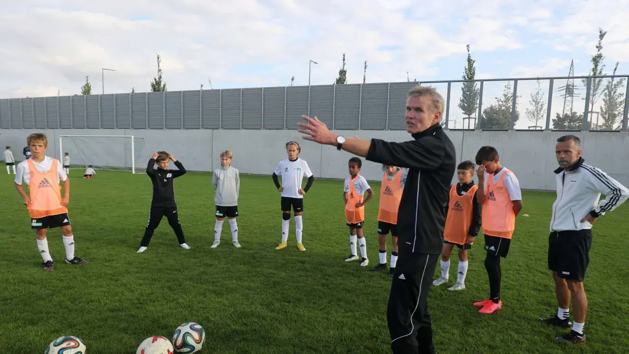 Trainer erklärt jungen Fußballern auf dem Feld Taktiken, die für ein DFB Duales Studium relevant sein könnten.