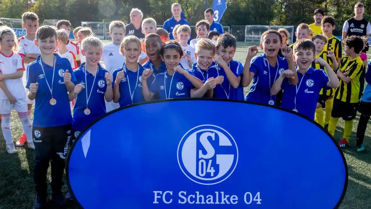 Junge Fußballer der Schalke U10 jubeln mit Medaillen vor einem Banner des FC Schalke 04.