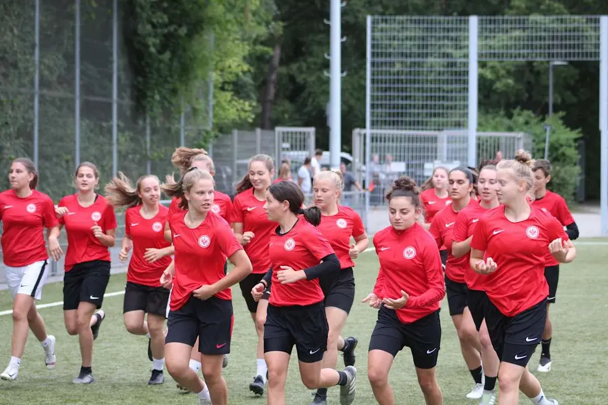 Eine Gruppe junger Fußballerinnen der u17 Juniorinnen im roten Trikot läuft auf einem Kunstrasenplatz.