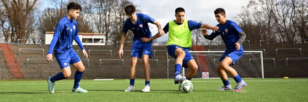 Vier junge Fußballer im C-Jugend-Training üben auf dem Kunstrasen. Einer dribbelt den Ball, die anderen verteidigen.