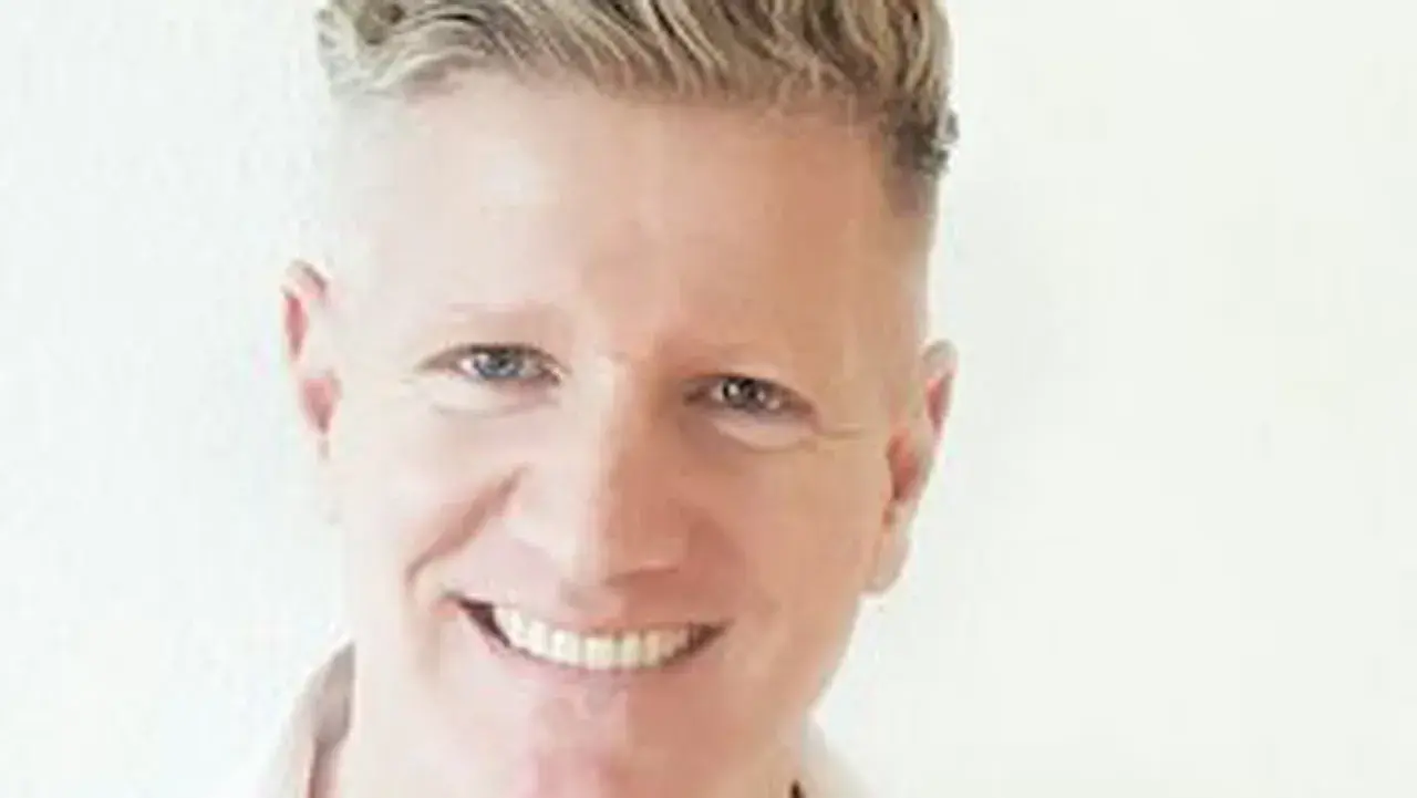 Ein Mann mit blondem Haar lächelt. Er könnte ein Sportpsychologe sein, der Athleten hilft, ihre mentale Stärke zu entwickeln.