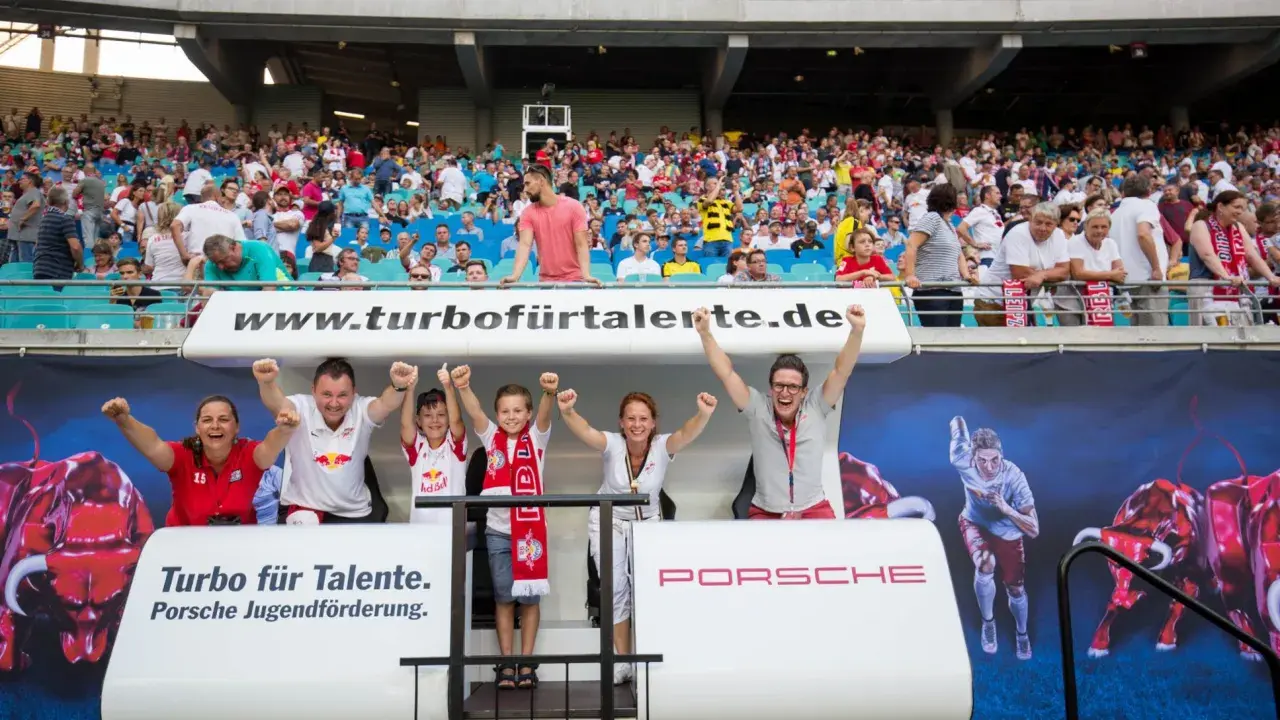 Familie jubelt bei einem Spiel der RB Leipzig U11. Die Fans tragen Trikots und Schals des Vereins.