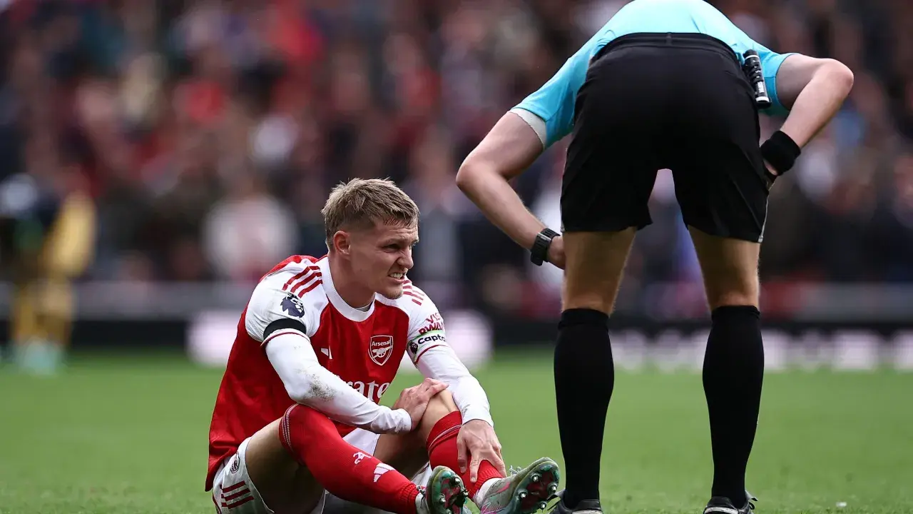 Martin Ødegaard sitzt verletzt auf dem Rasen, während ein Schiedsrichter ihn beobachtet.