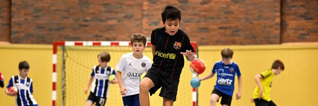 Jungen in Sporttrikots spielen Staffelspiele mit Ball in einer Sporthalle.