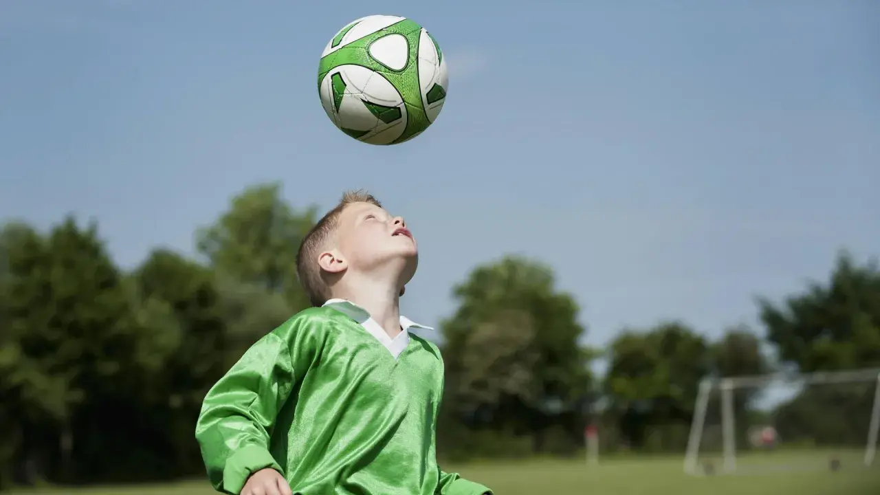 Junge im grünen Trikot übt den Kopfball. Der Ball schwebt über ihm, bereit für den perfekten Treffer.