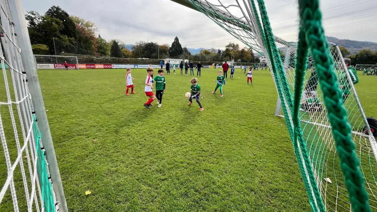 Kinder trainieren auf einem funino feld. Ein Junge im gr&uuml;nen Trikot dribbelt den Ball, w&auml;hrend andere Kinder auf dem Rasen spielen.