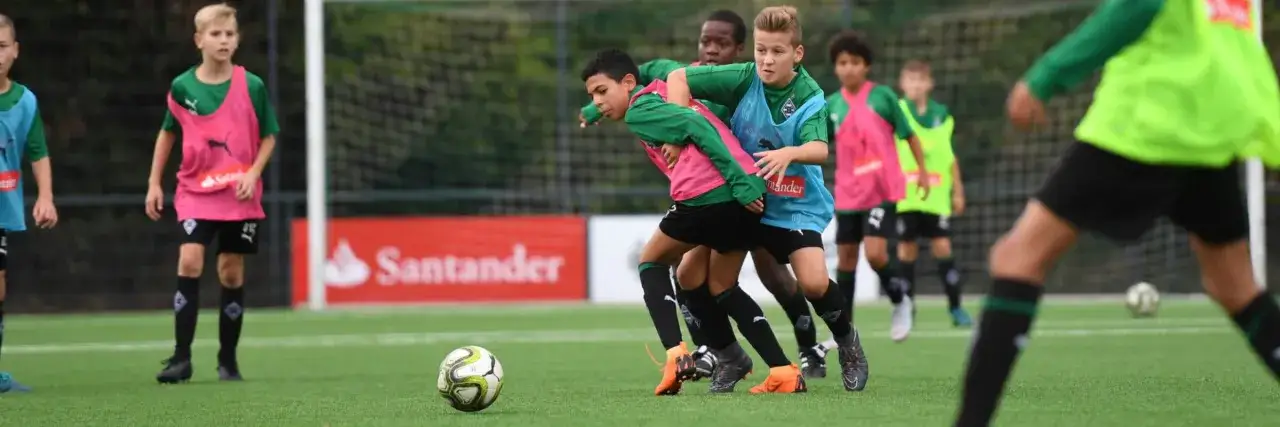 Jungs im Fu&szlig;balltraining k&auml;mpfen um den Ball. Sie tragen gr&uuml;ne Trikots und bunte Leibchen.