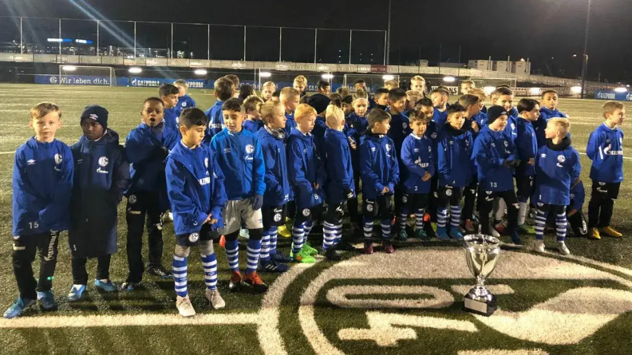 Die Schalke U10 feiert einen Sieg mit ihrem Pokal. Die jungen Fußballer tragen stolz ihre blauen Trikots.