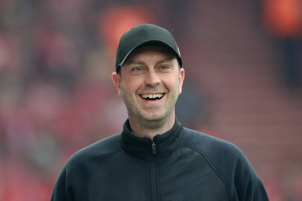 Lachender RB Leipzig Trainer mit schwarzer Kappe und Jacke, bereit f&uuml;r das n&auml;chste Spiel.