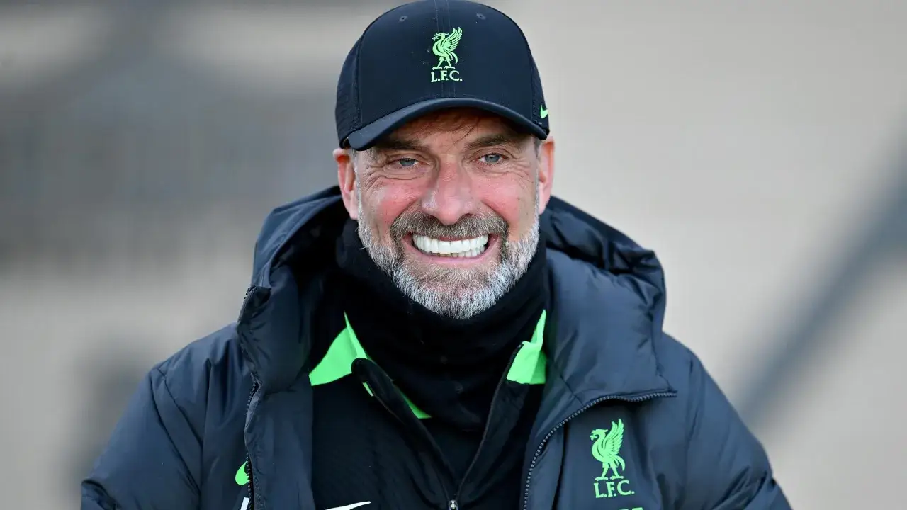 Trainer Klopp l&auml;chelt breit in die Kamera, tr&auml;gt eine schwarze Kappe mit dem LFC-Logo und eine dunkle Jacke.
