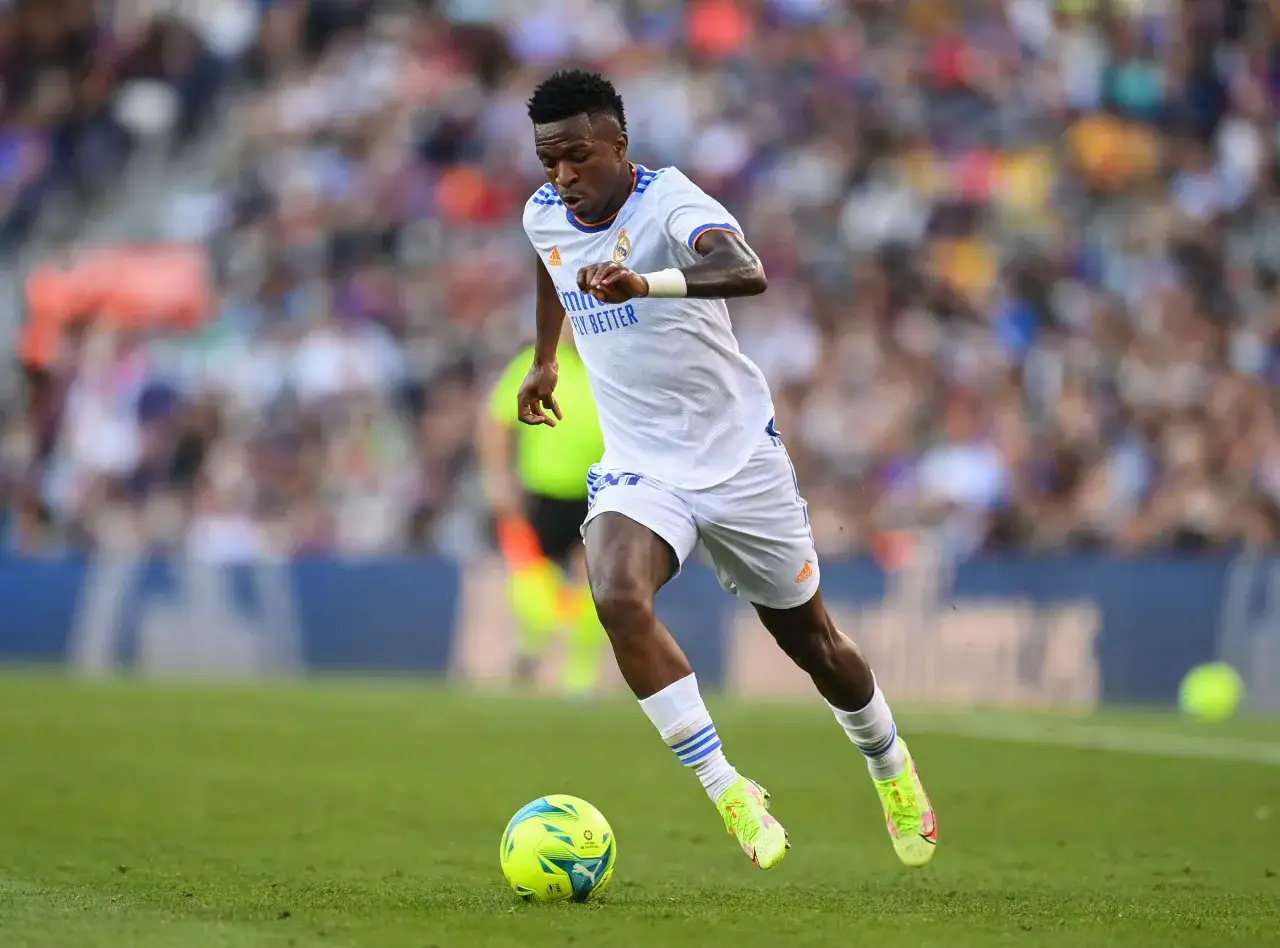 Vin&iacute;cius J&uacute;nior dribbelt im wei&szlig;en Trikot &uuml;ber den Rasen, der Ball am Fu&szlig;.