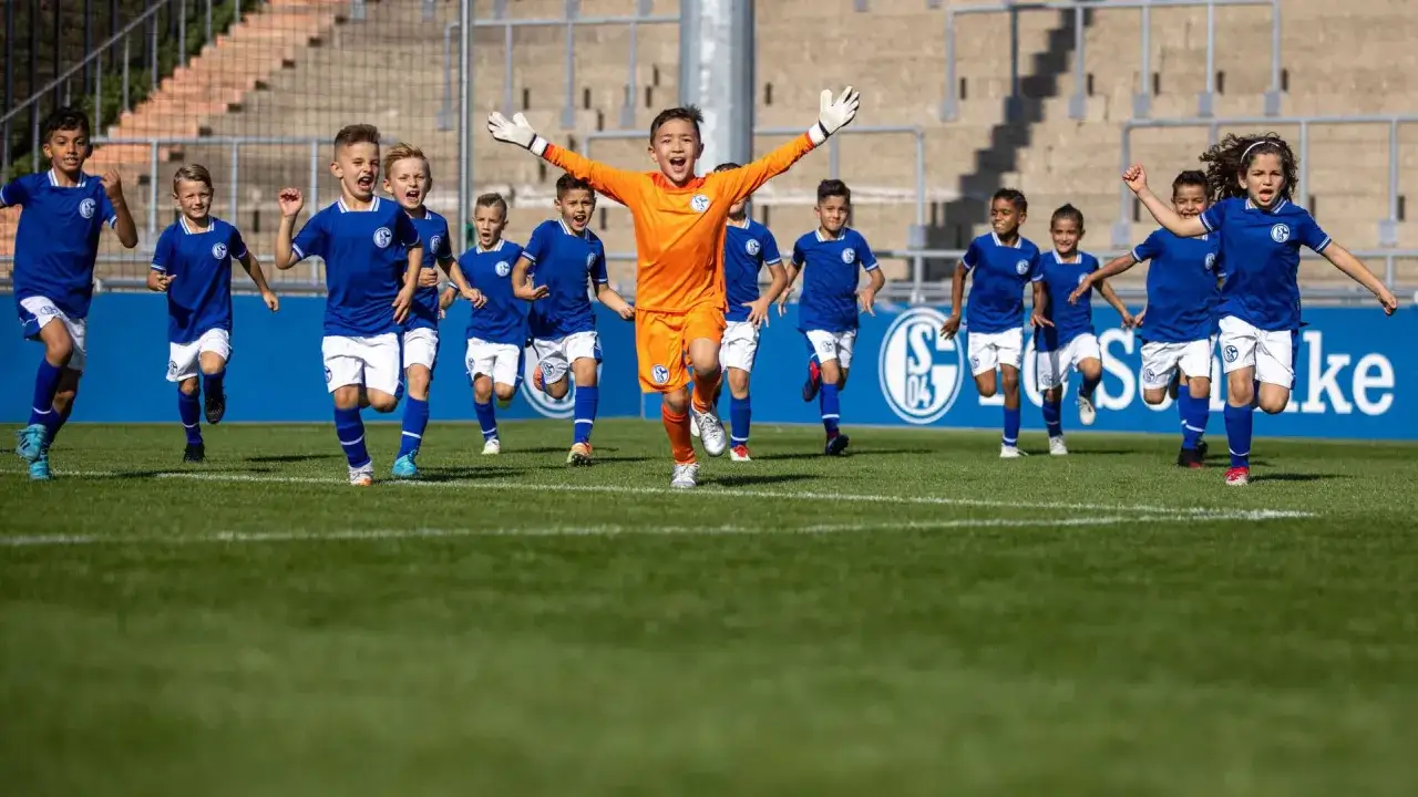 Junge Fußballer der Schalke U15 rennen jubelnd über den Rasen. Ein Torwart in orangefarbener Kleidung führt die Gruppe an.