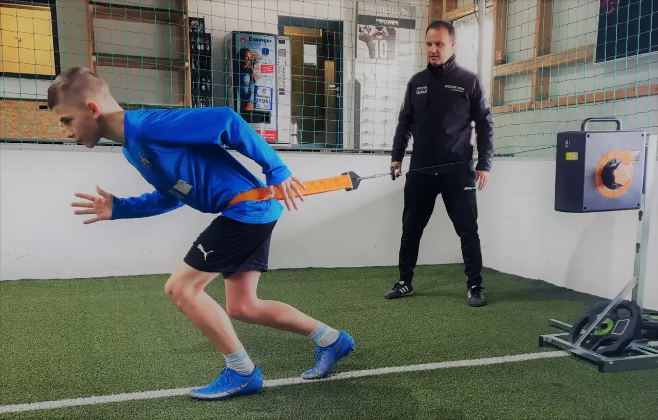 Junger Fu&szlig;baller im Sprint mit Widerstandsband, Trainer &uuml;berwacht das schnellkraft training.