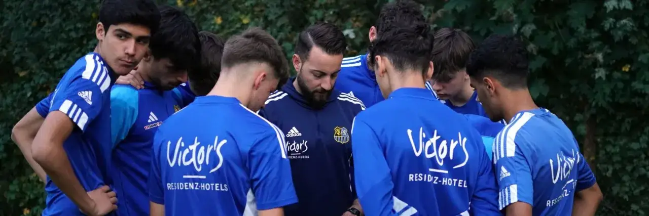 Jugendfußballer im Kreis versammelt, Trainer spricht. Ein Moment der Konzentration vor dem nächsten Spiel.