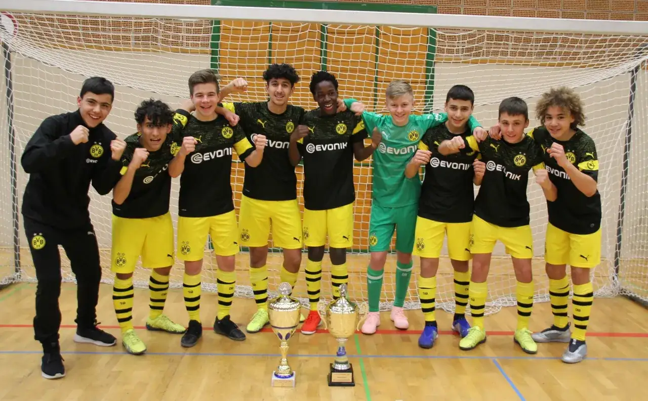 Junge Fu&szlig;baller der BVB U14 jubeln mit Pokalen.