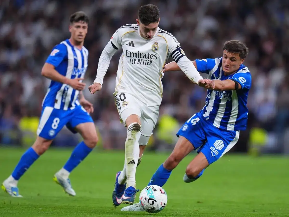Federico Valverde kämpft im weißen Trikot um den Ball, während zwei Gegner in blauen Trikots ihn bedrängen.