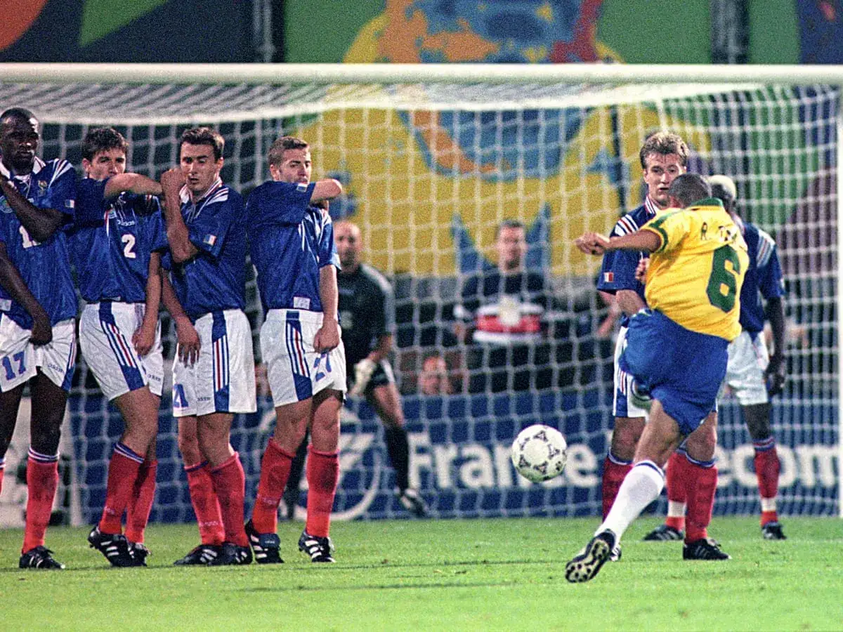 Brasiliens Roberto Carlos schießt den Ball mit unglaublicher roberto carlos schuss geschwindigkeit auf das Tor. Französische Spieler bilden eine Mauer.