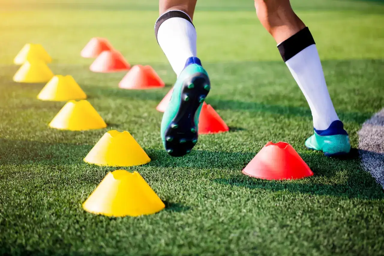 Fu&szlig;baller trainiert mit H&uuml;tchen auf dem Rasen. Schnelle Bewegungen und pr&auml;zise Schritte sind Teil des SAQ Trainings.