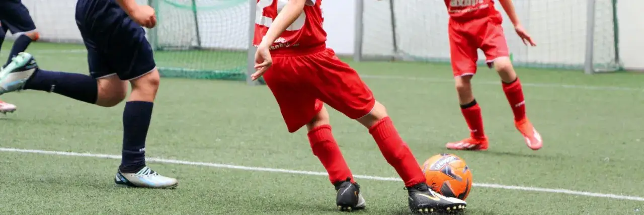 Kinder im Fu&szlig;balltraining &uuml;ben das Passen. Ein Ball liegt auf dem Kunstrasen, die Beine der jungen Spieler sind in Aktion.