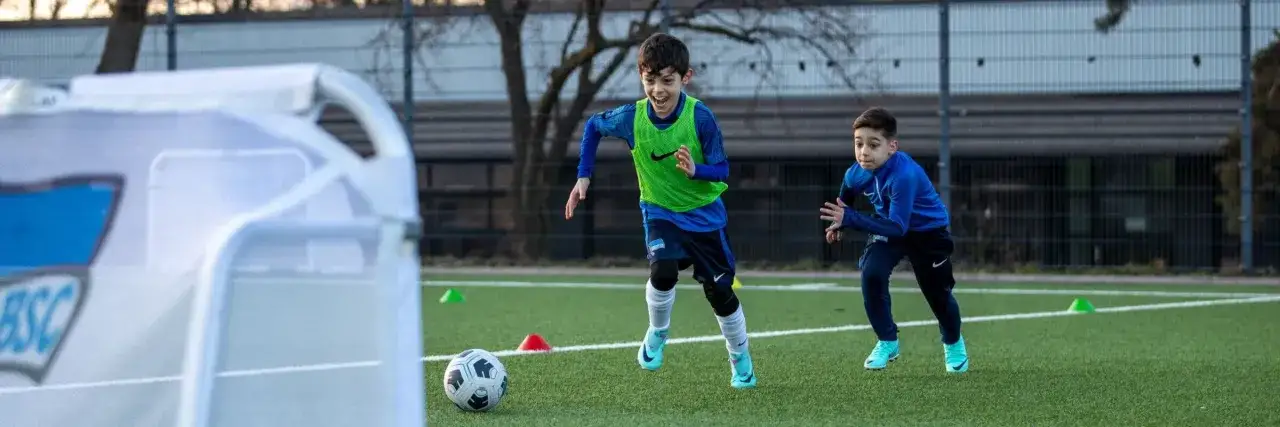 Zwei junge Fu&szlig;baller im Trainingsanzug sprinten &uuml;ber den Kunstrasen. Ein Trainingsplan f&uuml;r Junioren wird hier offensichtlich umgesetzt.