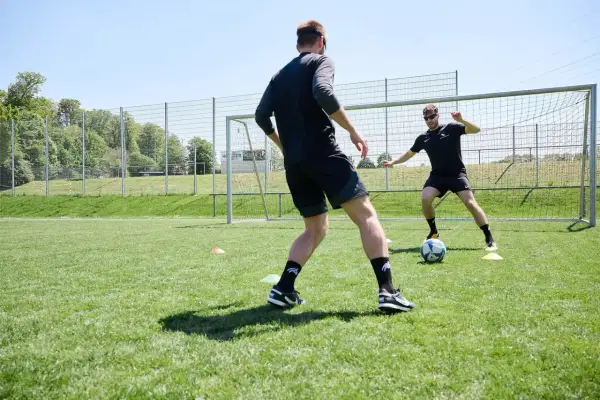 Zwei Fußballer trainieren auf einem Rasenplatz. Der Fokus liegt auf dem neurozentrierten Training, um Koordination und Reaktionsfähigkeit zu verbessern.