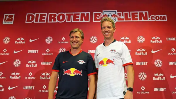 Julian Nagelsmann und ein Kollege posieren vor der roten Kulisse von RB Leipzig.